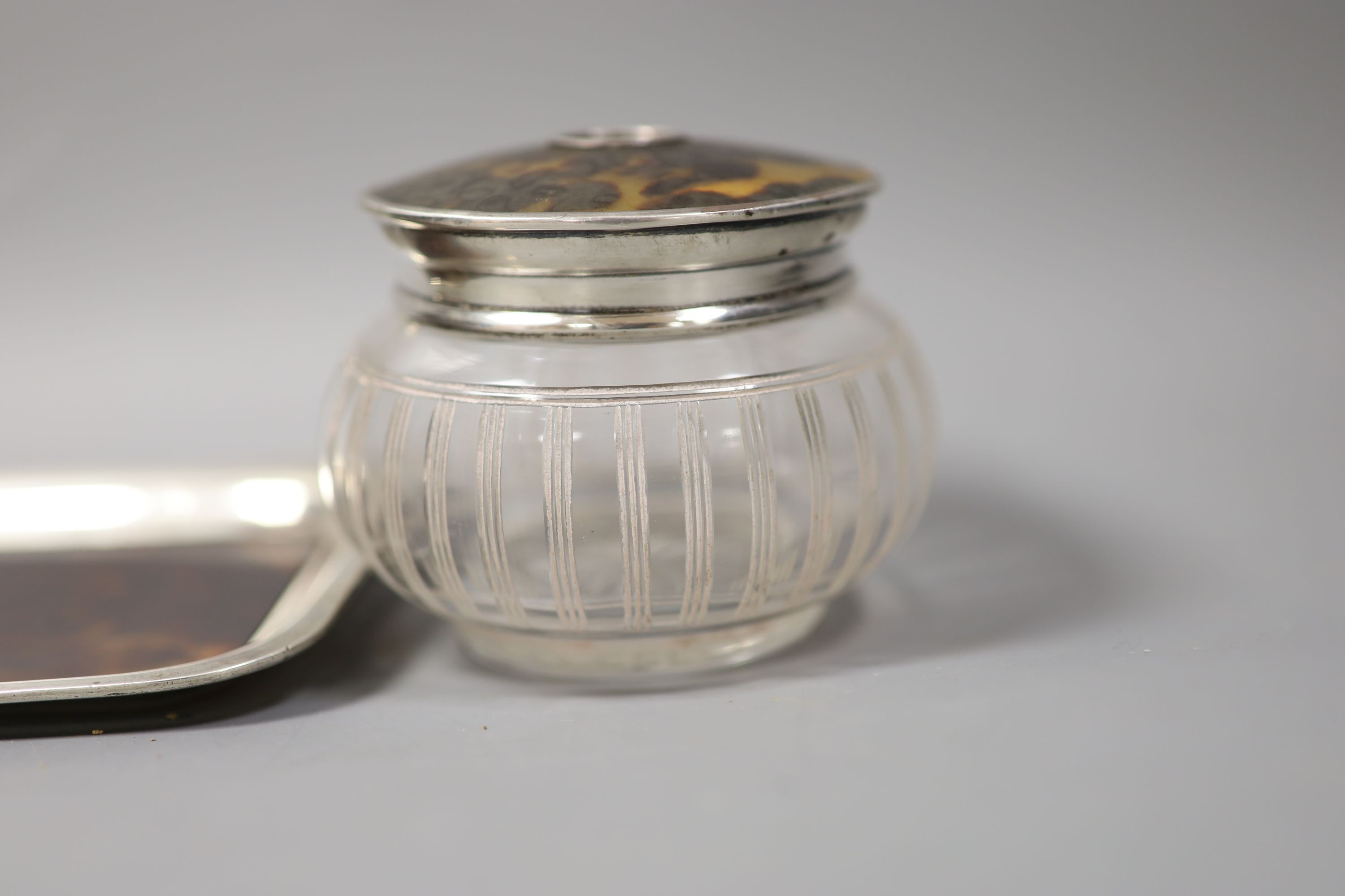 An Edwardian silver mounted tortoiseshell dressing table tray and a similar mounted glass tidy.